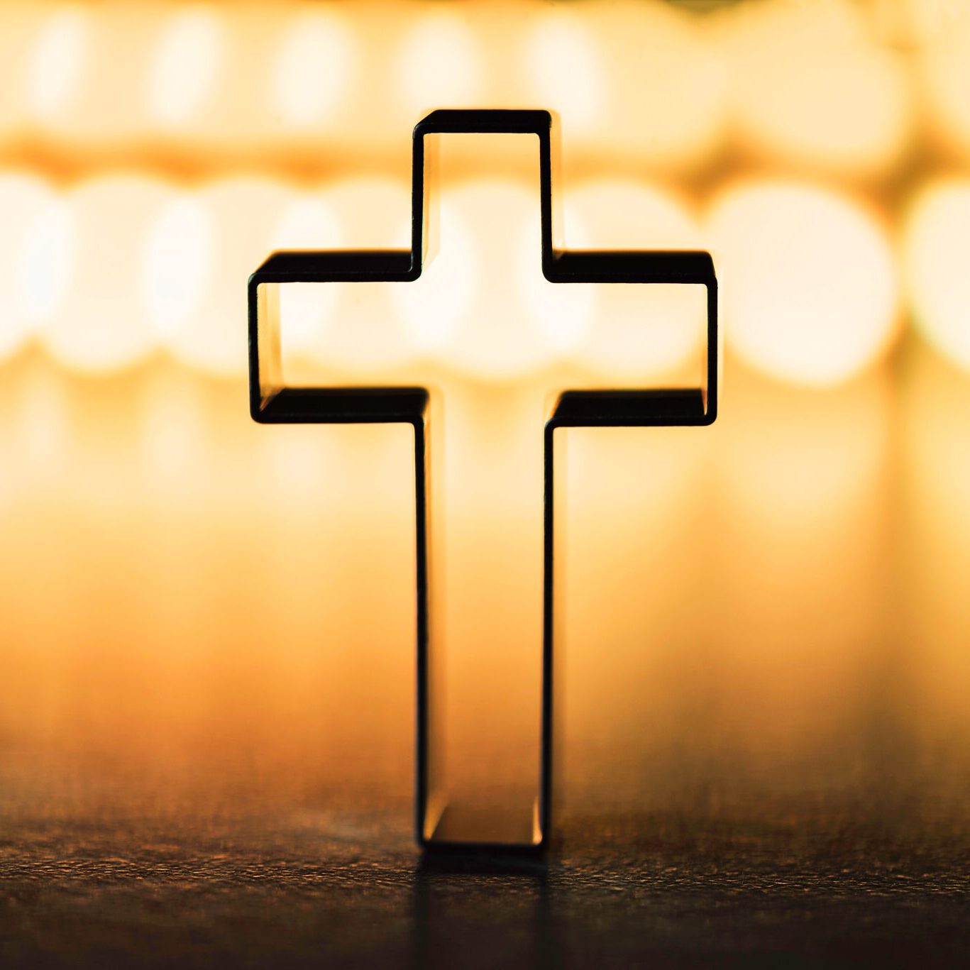 Silhouette of christian cross on yellow background, soft bokeh lights background. Copy space. Church worship, salvation concept. Faith symbol in Jesus Christ. Holy cross for Christmas, Easter day.